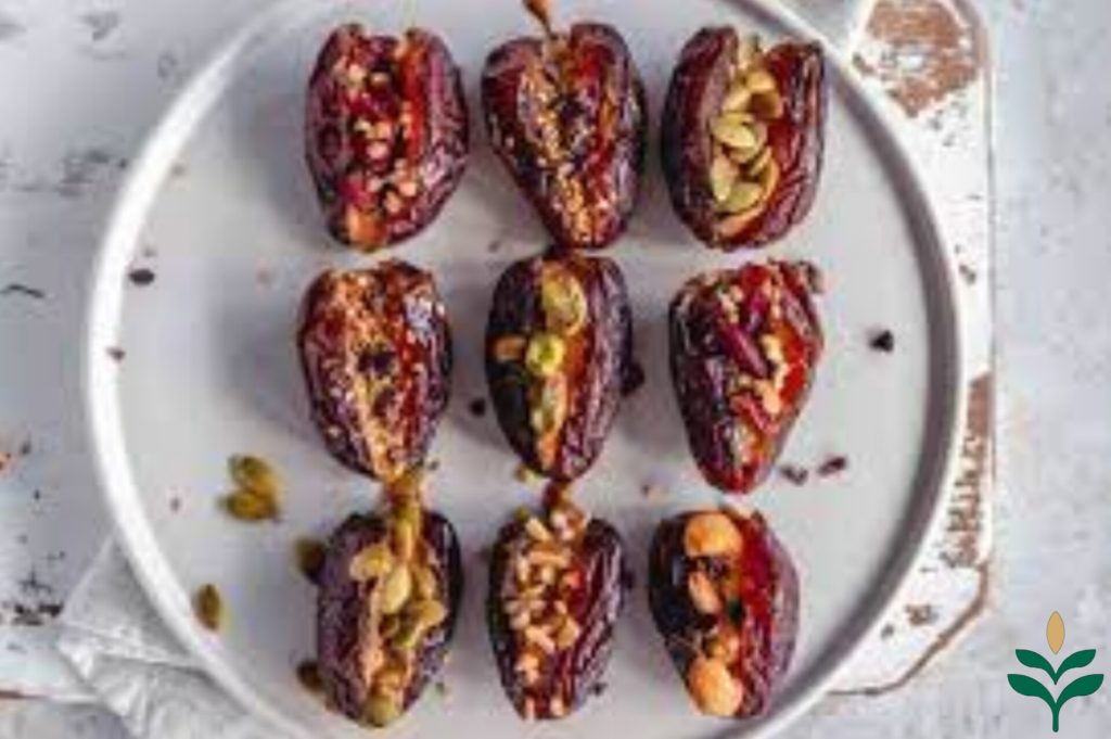 6 دانه خرمای پیارم پر شده با انواع مغزهای پسته، بادام، کنجد و آفتاب گردان روی یک بشقاب سرامیک سفید