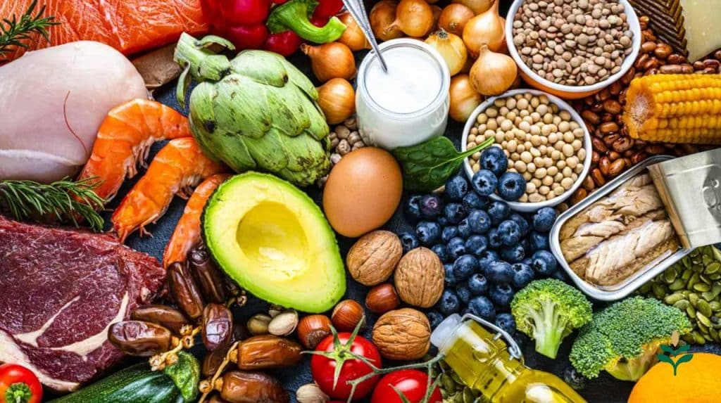 The image shows a wide range of foods commonly used in the Mediterranean diet, such as walnuts, hazelnuts, dates, blueberries, broccoli, tuna, yogurt, lentils, chickpeas, artichokes, red meat, chicken breast, corn, peas, and onions.