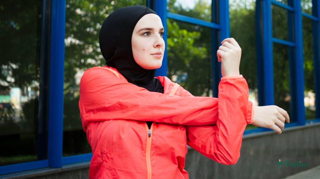 A woman wearing a hijab doing stretching exercises on her hands and arms.