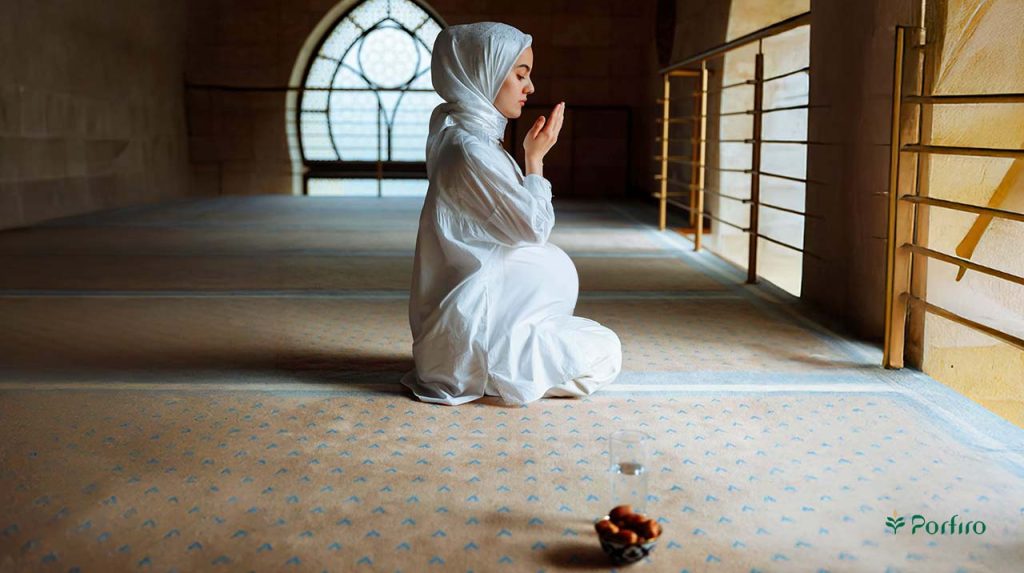 A pregnant woman is praying in a white dress, and a glass of water and a small bowl of dates are also seen nearby.
