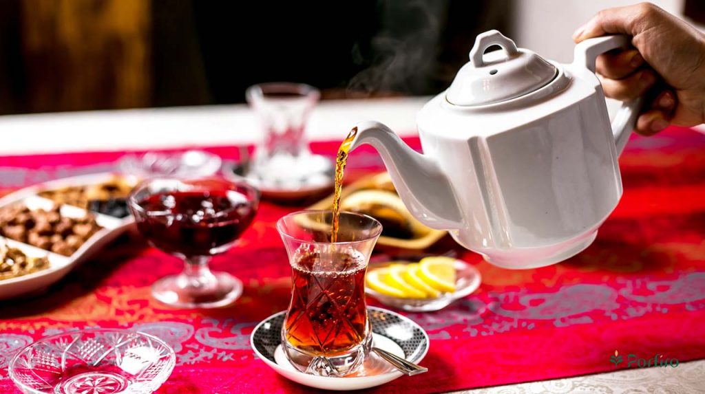 سفره صبحانه ایرانی و دستی که در حال ریختن چای ایرانی از قوری سفید چینی در استکان شیشه ای