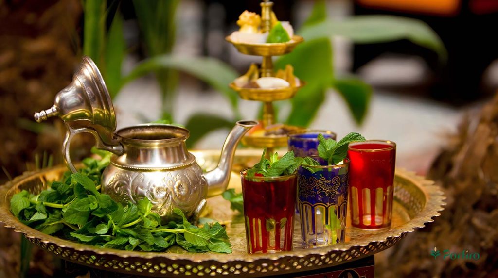 چهار لویان سنتی در دور رنگ آبی و قرمز با یک قوری فلزی و مقدری نعناع در کنار آن که همه روی یک سینی فلزی قرار گرفته اند و آماده دم کردم جای مراکشی هستند
