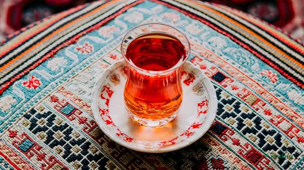 یک استکان با زیر آن که حاوی چای قرمز است و روی فرش ایرانی قرار گرفته است
