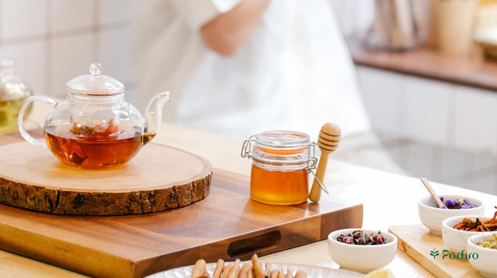 یک قوری شیشه ای حاوی چای در کنار یک ظرف پر از عسل