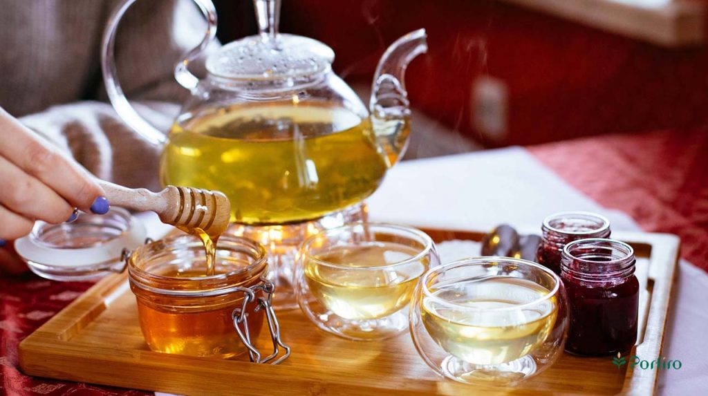 دو فنجان چای سبز با یک ظرف عسل و قوری پر از چای در یک سینی که دو ظرف مربا هم در کنار آنها دیده می شود