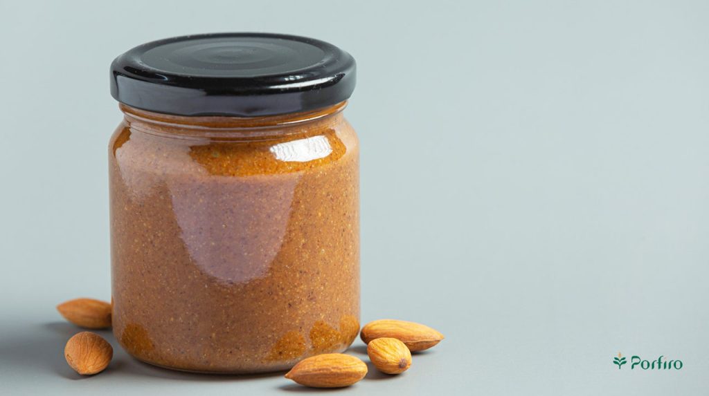 A glass container with a metal lid containing almond paste and a few almond kernels next to it