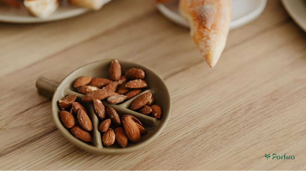 A small olive-colored bowl containing Iranian almond kernels on the table.
