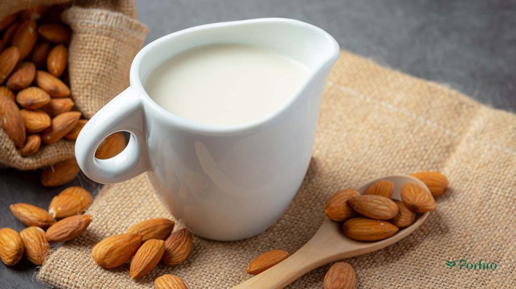 A sauce container containing thick almond milk and a spoon with a few almond kernels in it.