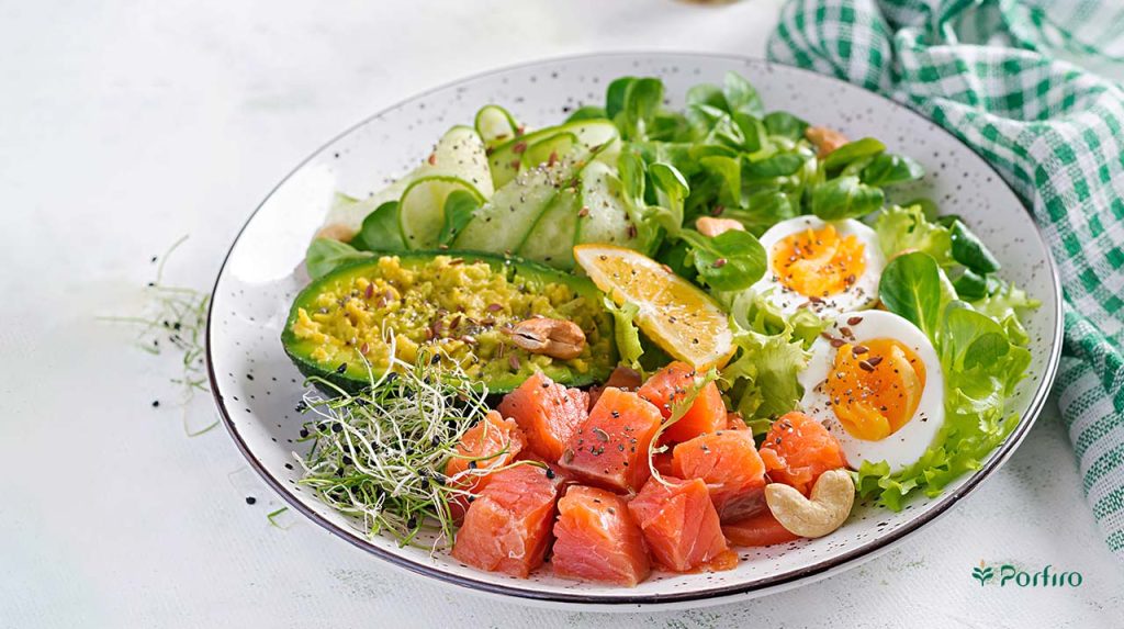 A plate of food containing lettuce, boiled egg, fish, avocado, cucumber and a slice of lemon