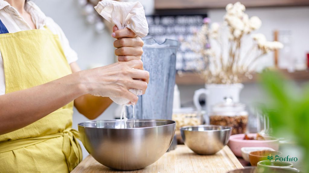 Midsection of a woman using her hands to squeeze a strainer containing a mixture of almonds and water to make almond milk