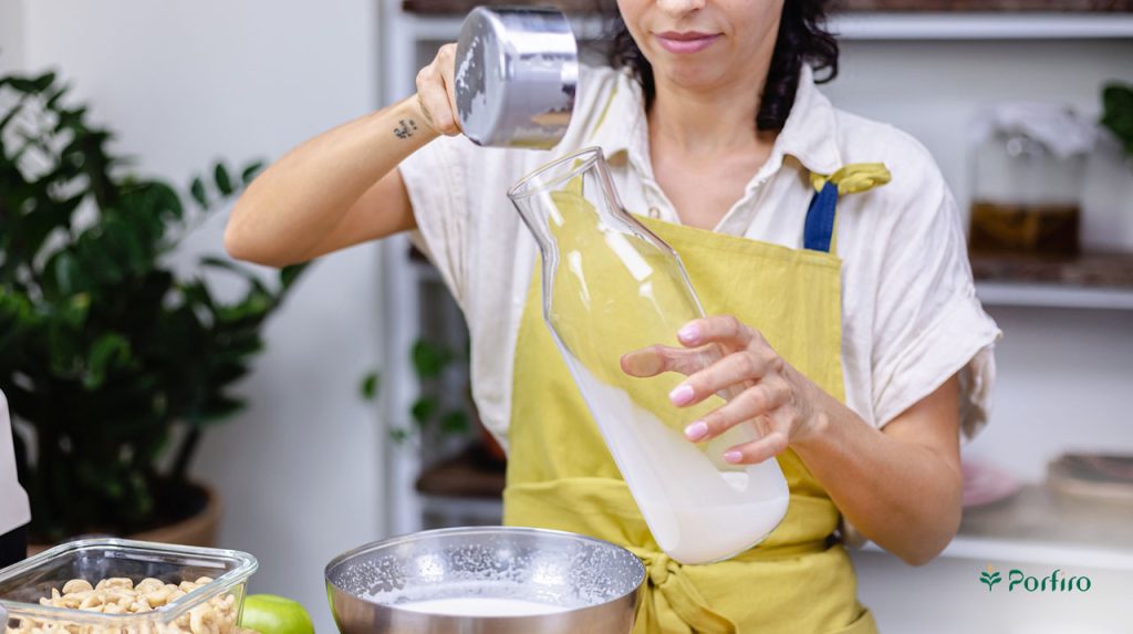 The final stage of preparing almond milk by a woman pouring the obtained almond milk into a pitcher.