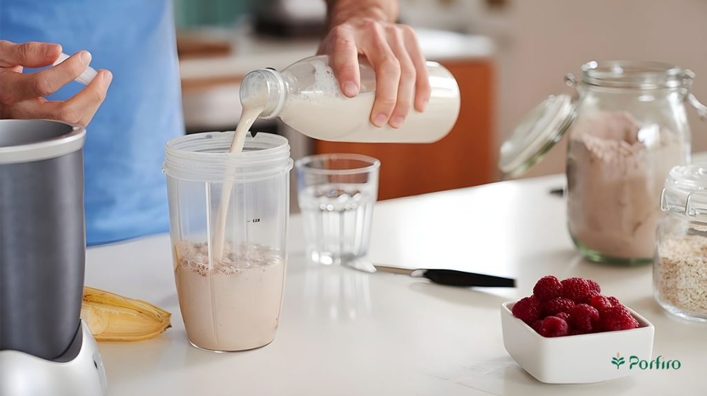 A person is making a protein shake and pouring milk into it.