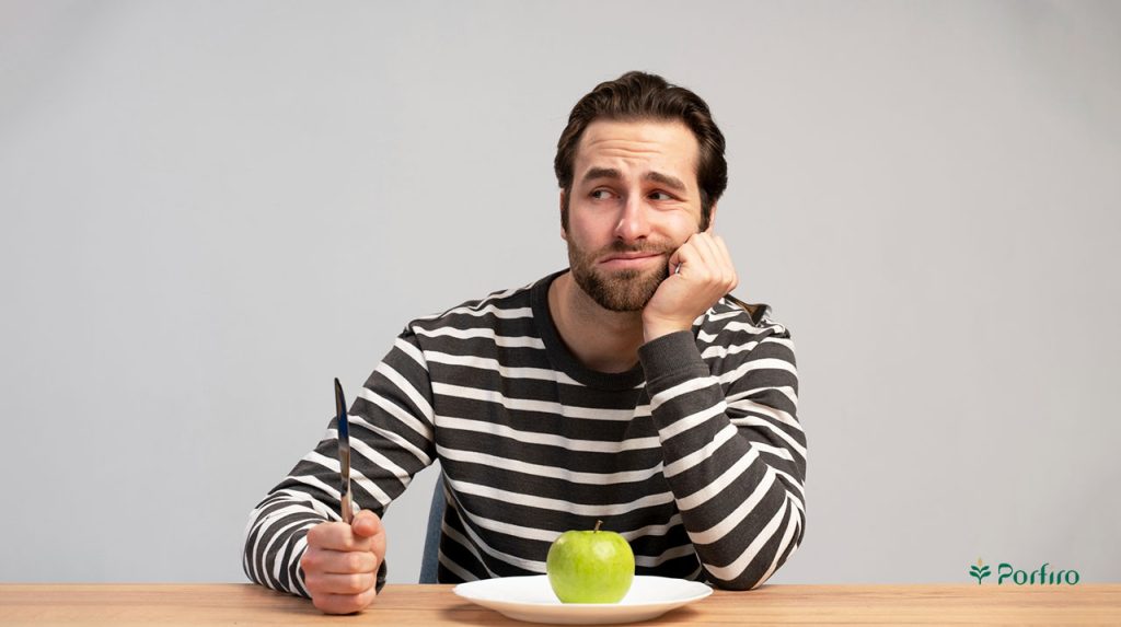 A person is sitting at a table with a plate containing how many apples in front of him, and he is reluctant to eat with a fork in his hand.
