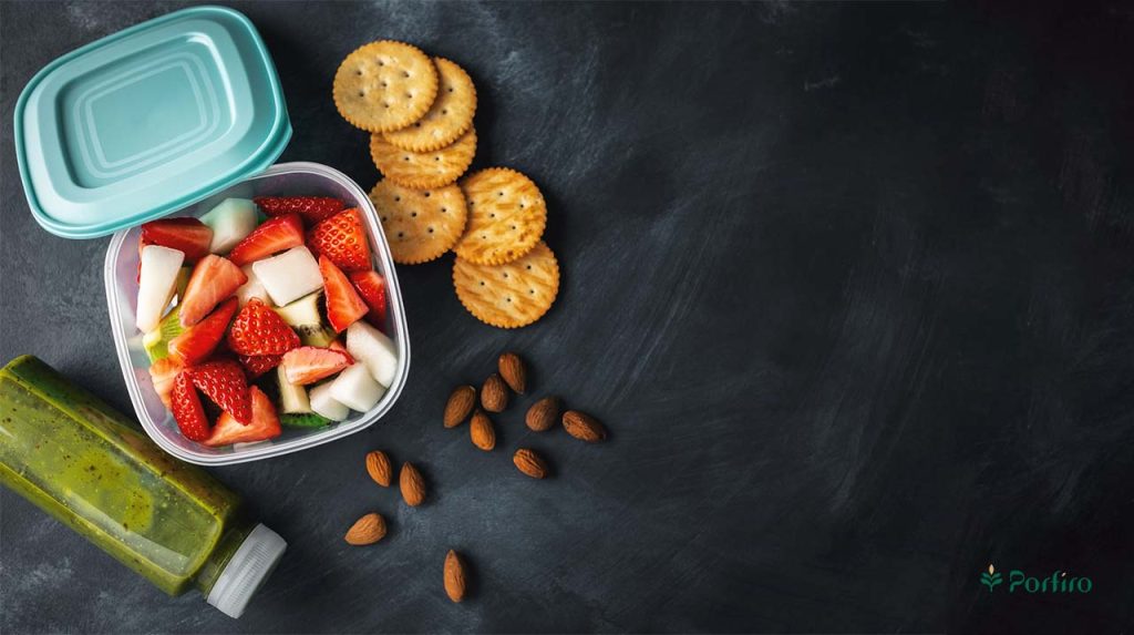 A green drink, a bowl of chopped fruit, some biscuits and some almonds in the left corner with a black background