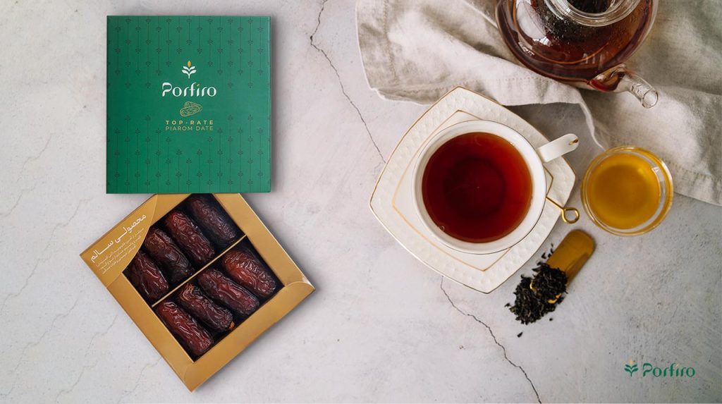 یک بسته نیمه باز خرمای پیارم پرفیرو در کنار یک فنجان چای سیاه و قوری شیشه ای