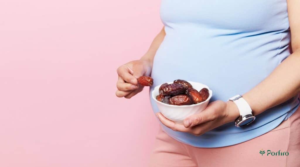 A pregnant woman is picking a date from a bowl full of dates in her hand.