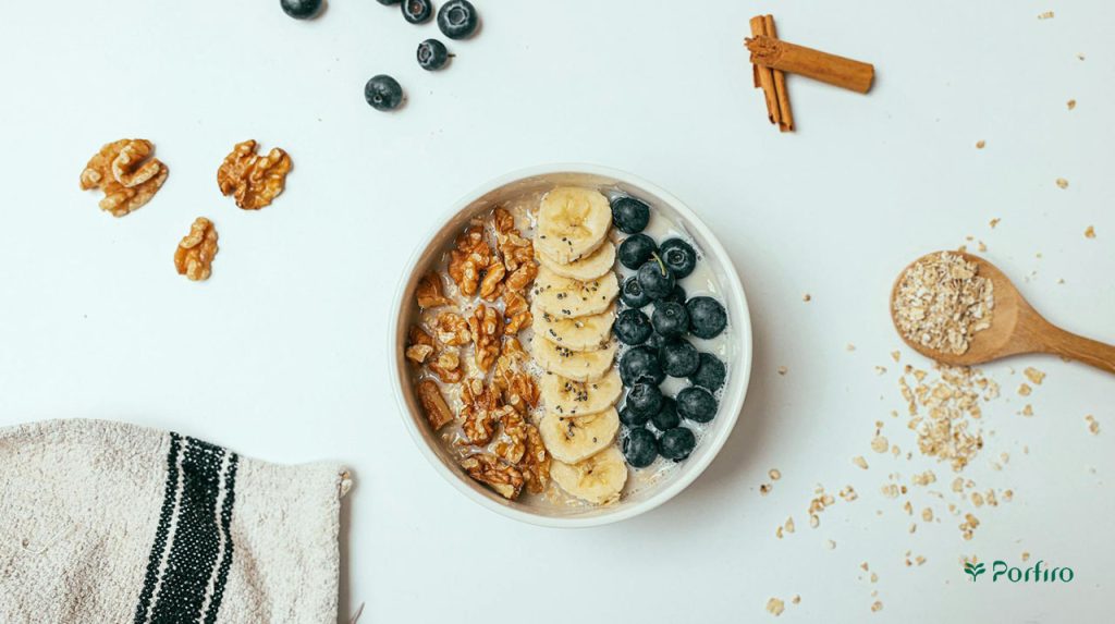 A bowl of oatmeal prepared with various ingredients such as blueberries, bananas, and walnuts in the article Health Benefits of Nuts and Seeds on the Porfiro Blog
