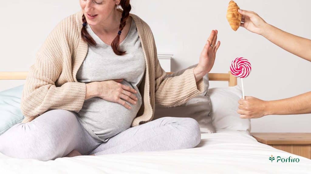 Pregnant woman sitting in her bed and passing out croissants and candy in an article on nutrition during pregnancy