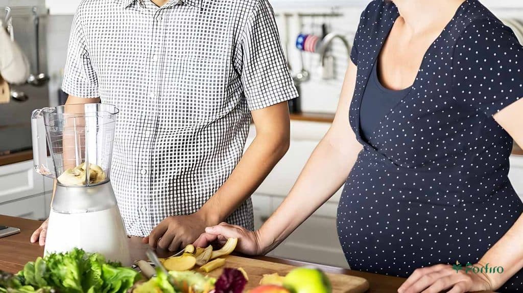 Pregnant woman and man preparing food using fruits and vegetables in the kitchen