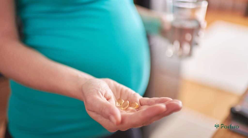 A pregnant woman holds several supplements and a glass of water in her hands in the article Nutrition during pregnancy