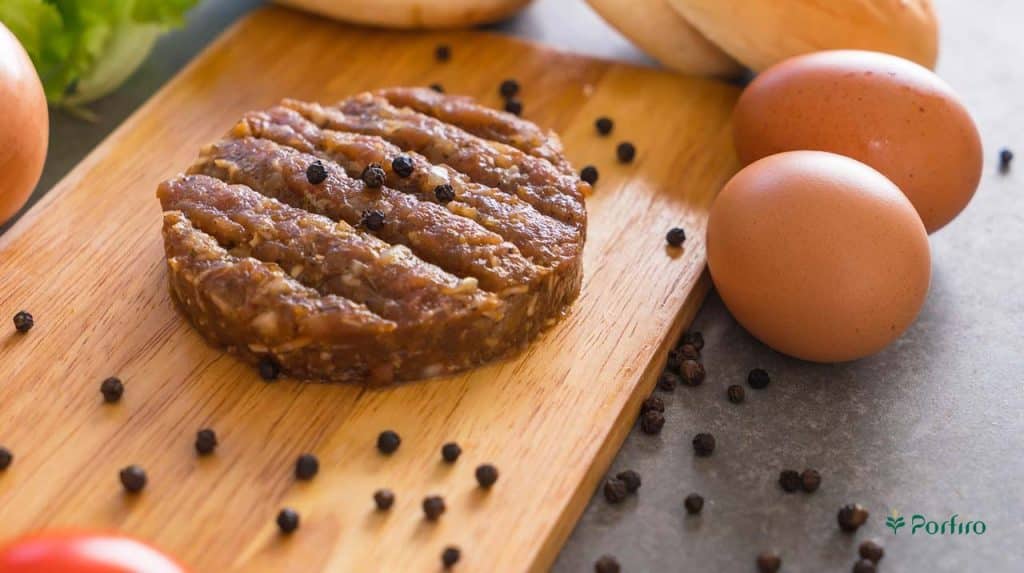 A fresh, unfried hamburger on a kitchen board next to two eggs