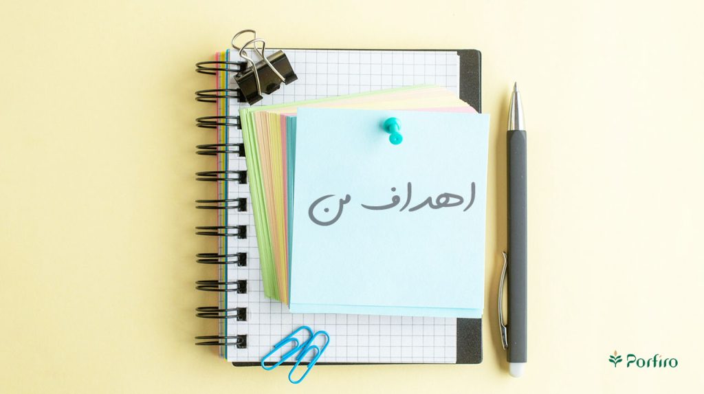 یک خودکار و دفترچه یادادشت و برگه ها نت رنگی که روی یکی از آنها نوشته شده است: اهداف من