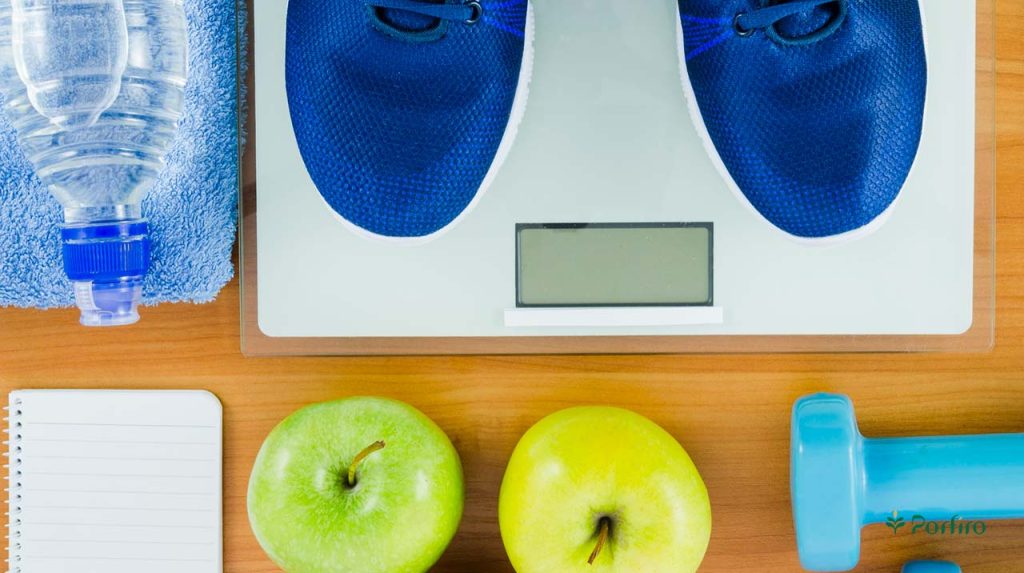 Measuring weight with a scale and two apples and dumbbells next to it