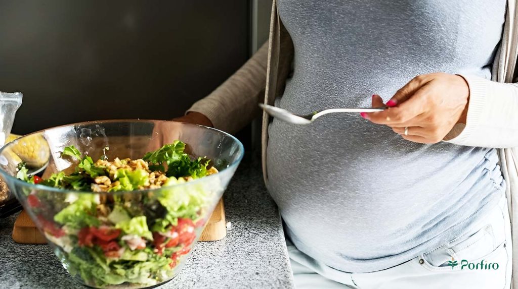 خانم باردار در کنار ظرف غذایی حاوی مواد غذایی گیاهی در آشپزخانه