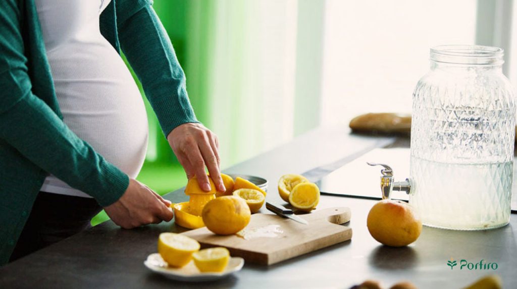 خانم باردار در حال آماده کردن شربت آبلیمو با استفاده از لیموهای تازه در محیط آشپزخانه