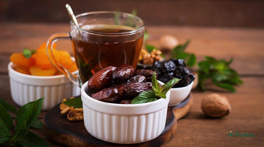 A bowl of dates next to a glass of tea and bay leaves