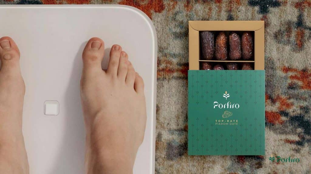 A person's feet on a scale and a package of Piarom Porfiro dates next to it to show weight gain as a side effect of consuming too many dates.