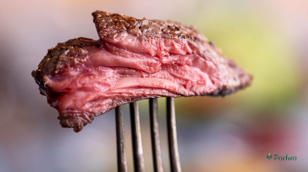 A slice of undercooked meat on a fork that can cause food poisoning