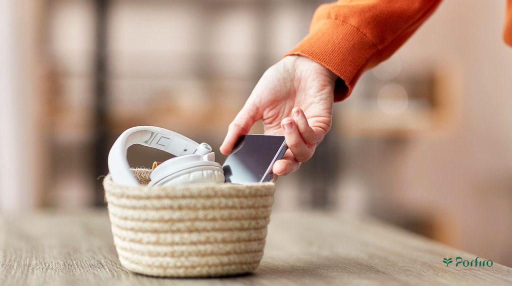 A person's hand putting their phone in a wicker basket to use it less.