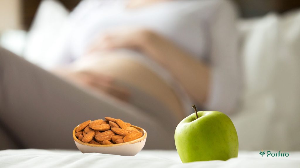 Pregnant woman in the background with a green apple and a bowl of almonds in front of her