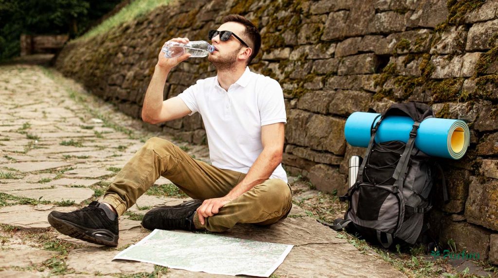 Young man sitting on the floor studying a travel map and drinking water.